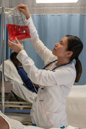 Nursing student hanging IV bag on pole.