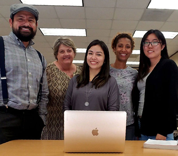 Group of people standing in front of a MacBook laptop.