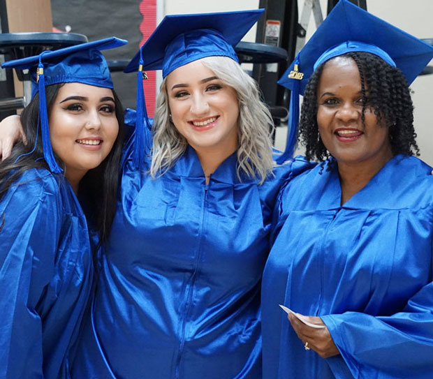 Three female students in blue regalia at graduation.