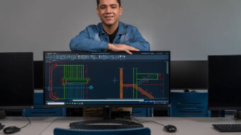 Student Jose Lopez standing behind monitor with drafting designs on the screen