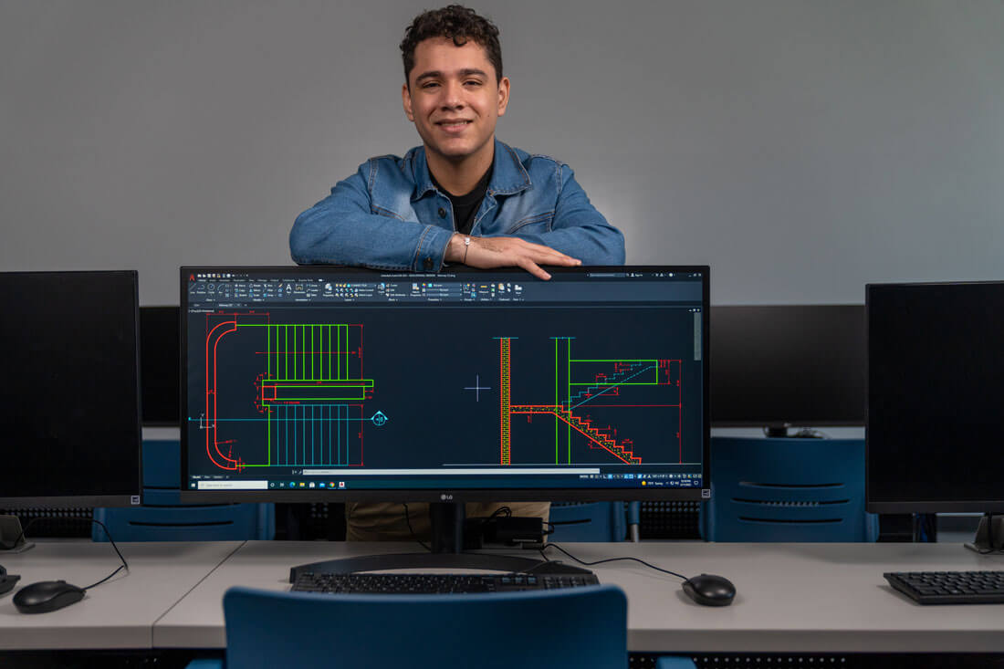 Student Jose Lopez standing behind monitor with drafting designs on the screen
