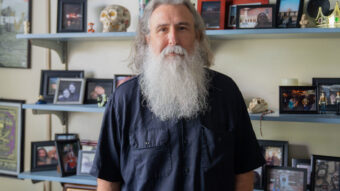 PHOTO: COM Professor Bernie Smiley poses for a portrait in his office, surrounded by personal belongings, photographs and more on shelves in the background.