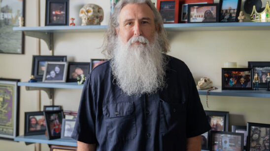 PHOTO: COM Professor Bernie Smiley poses for a portrait in his office, surrounded by personal belongings, photographs and more on shelves in the background.