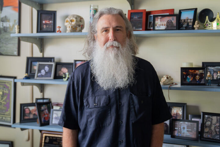 PHOTO: COM Professor Bernie Smiley poses for a portrait in his office, surrounded by personal belongings, photographs and more on shelves in the background.